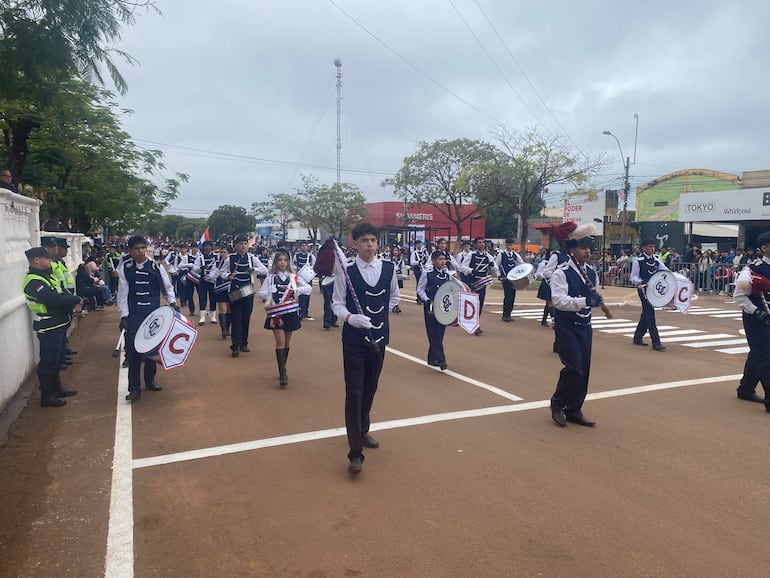 Estudiantes en uniformes blanco y negro marchan con instrumentos, acompañados por policías en un ambiente festivo en Concepción.