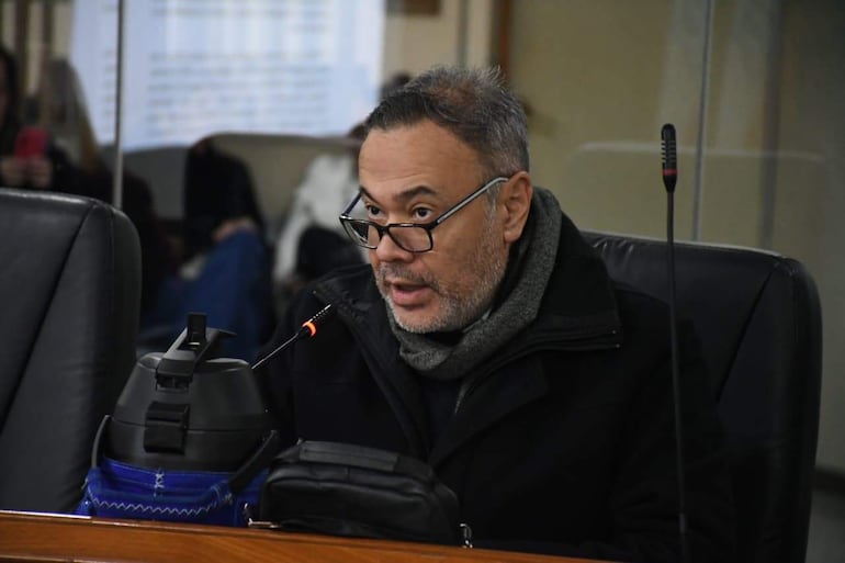 Humberto Blasco, con abrigo negro y bufanda gris, habla en un ambiente formal, rodeado de asistentes en un tribunal.