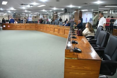 Rosanna Rolón sonríe mientras discute, rodeada de personas en un ambiente formal con mobiliario de madera.