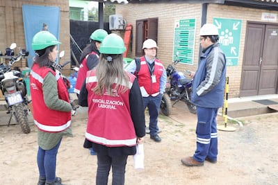 Grupo de fiscalizadores en chalecos rojos conversan en exterior con teléfonos, junto a motocicletas y señalización de emergencia.