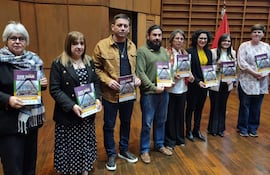 Seis personas alineadas en un auditorio, sosteniendo folletos de la revista. Mujer de cabello corto y canoso, hombre en camisa mostaza y mujeres con blusas de colores.