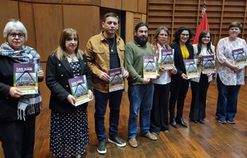 Seis personas alineadas en un auditorio, sosteniendo folletos de la revista. Mujer de cabello corto y canoso, hombre en camisa mostaza y mujeres con blusas de colores.