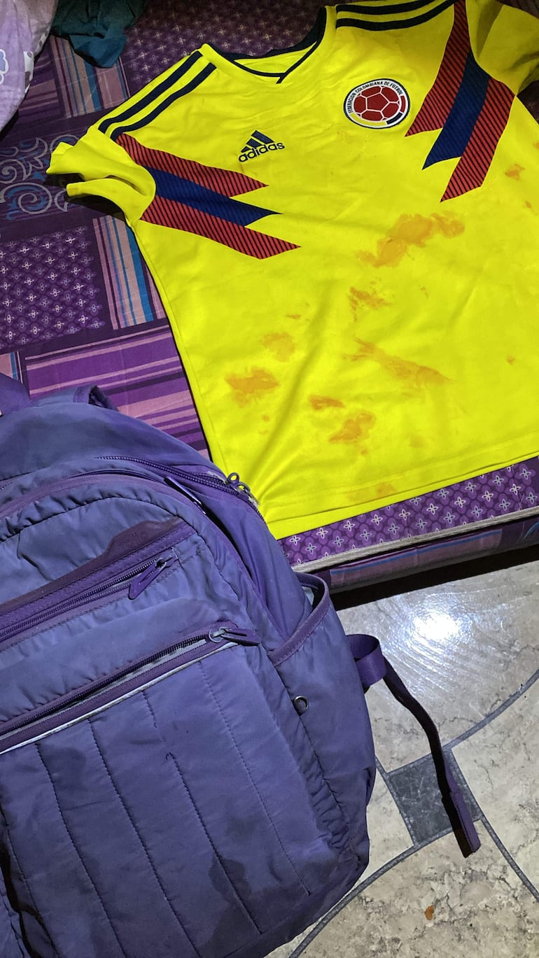 Camiseta amarilla de la selección colombiana de fútbol y mochila morada sobre una superficie colorida, sin personas visibles.