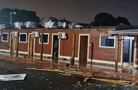 Estructura de ladrillo rojo con techo dañado y material esparcido en un ambiente exterior mojado.