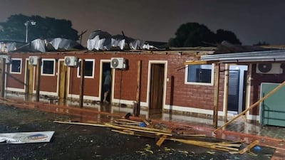 Estructura de ladrillo rojo con techo dañado y material esparcido en un ambiente exterior mojado.