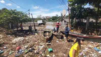 Niño con camiseta amarilla, joven con camiseta oscura y hombre con camiseta roja revisan daños tras inundaciones en un ambiente urbano.