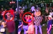 Hombre con sombrero grande y otro con gafas y camiseta roja, sonriendo en un ambiente animado de celebración.