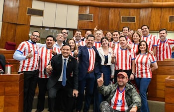 Diputados sonrientes, la mayoría con camisetas rojas y blancas, posando juntos en un ambiente legislativo.