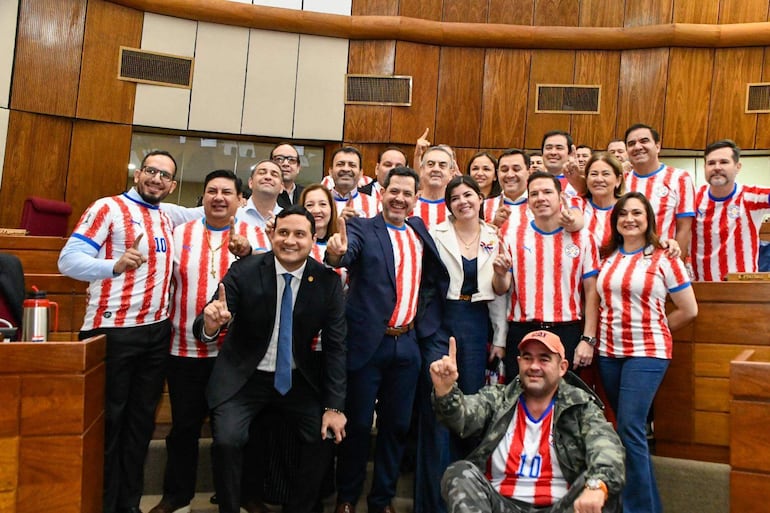 Diputados sonrientes, la mayoría con camisetas rojas y blancas, posando juntos en un ambiente legislativo.