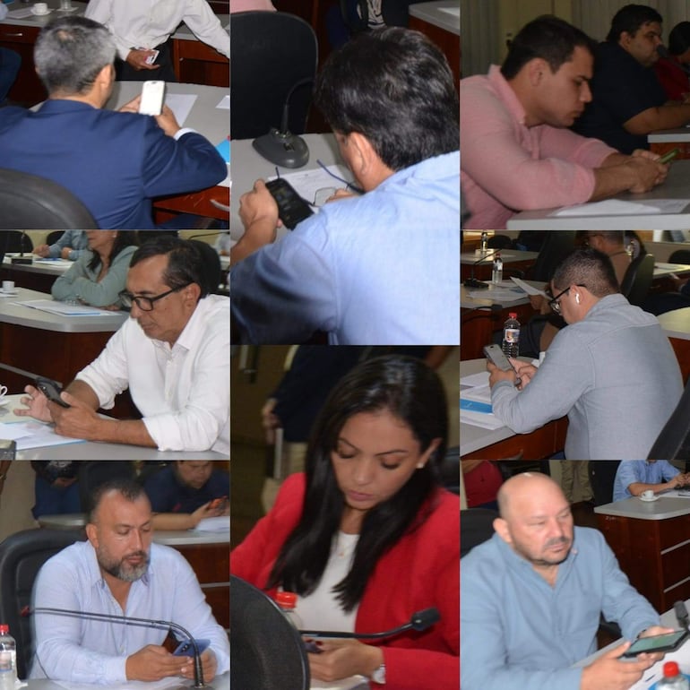 Ocho concejales en sala de reuniones, sentados y concentrados en sus teléfonos