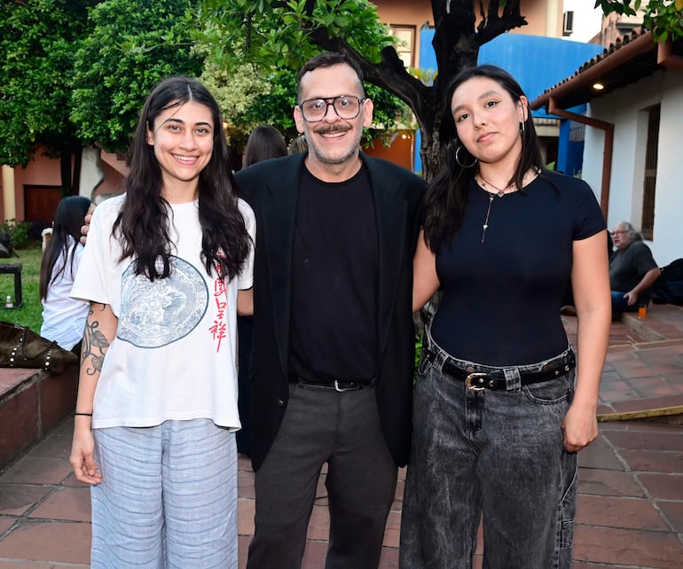 Dos mujeres y un hombre sonríen en un ambiente ajardinado, vistiendo ropa casual y moderna.