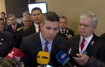 Peña en traje gris habla ante micrófonos, con oficiales militares escuchando en segundo plano.