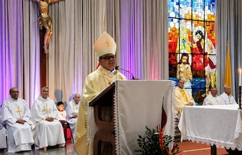 Monseñor Osmar López en vestimenta litúrgica dorada habla desde un podio mientras otros sacerdotes lo rodean en un altar decorado.