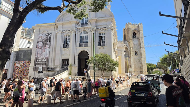 Multitud de turistas en la entrada del museo de Santo Antonio, algunos llevan sombreros y están relajados. Motocicleta de reparto en primer plano.