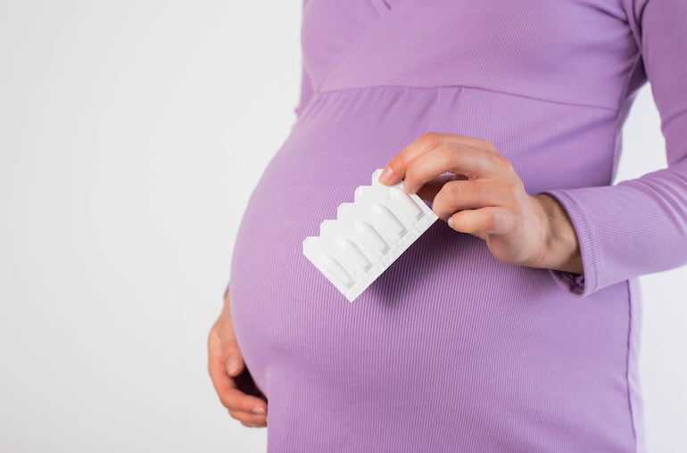 Mujer embarazada sostiene supositorios, concepto de hemorroides.