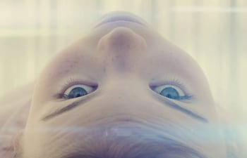 Primer plano de niño con ojos expresivos y piel clara, acostado en un entorno iluminado suavemente.