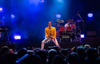 Cantante de 'Experiencia Queen' con chaqueta amarilla y pantalones blancos, sosteniendo un micrófono y emocionando a la multitud.