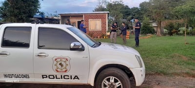 Policías con vestimenta de trabajo investigan un atraco en casa de ladrillo, con camioneta policial en primer plano y vegetación alrededor.