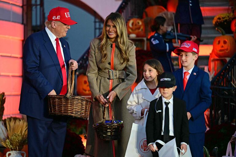 El presidente de Estados Unidos, Donald Trump, y la primera dama, Melania Trump, saludan a niños disfrazados de ambos, acompañados por un agente del Servicio Secreto, durante un evento de Halloween celebrado en la Casa Blanca en Washington, D.C. (Jim WATSON / AFP)