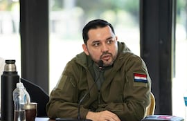 Luis Bello en chaqueta oliva con parche de Paraguay, hablando frente a un micrófono en un ambiente iluminado por luz natural.