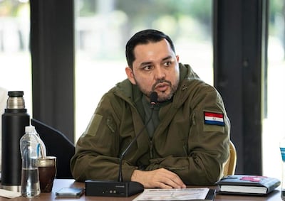 Luis Bello en chaqueta oliva con parche de Paraguay, hablando frente a un micrófono en un ambiente iluminado por luz natural.