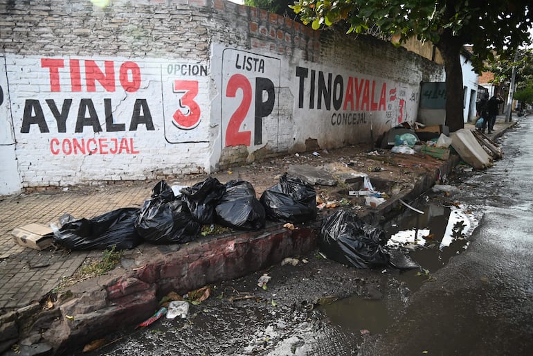 Mural electoral con las palabras 'TINO AYALA CONCEJAL' entre basura y escombros en la acera de una calle municipal.