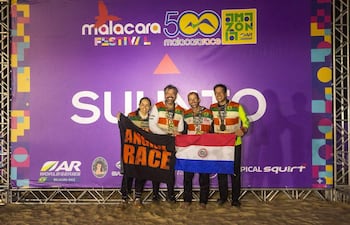 Cuatro miembros del equipo Angiru sonríen, vistiendo camisetas coloridas, sosteniendo banderas paraguaya y negra tras una competencia deportiva.