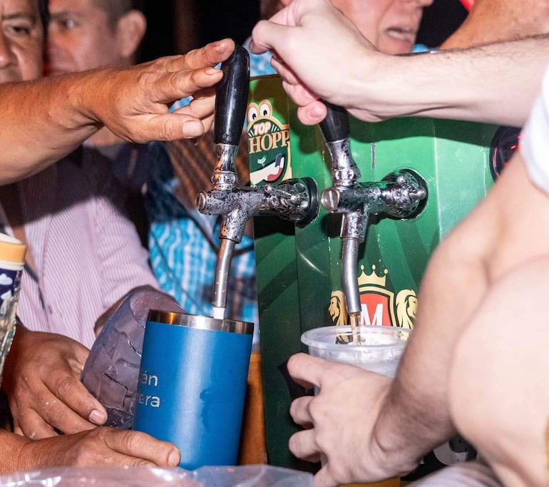 Varias manos interactúan con dispensador de cerveza mientras la gente disfruta del Choppfest en un ambiente animado al aire libre.