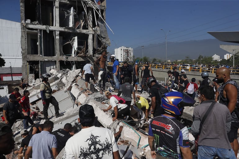 Personas caminan sobre los escombros de un edificio colapsado este lunes, en Cali, Colombia.