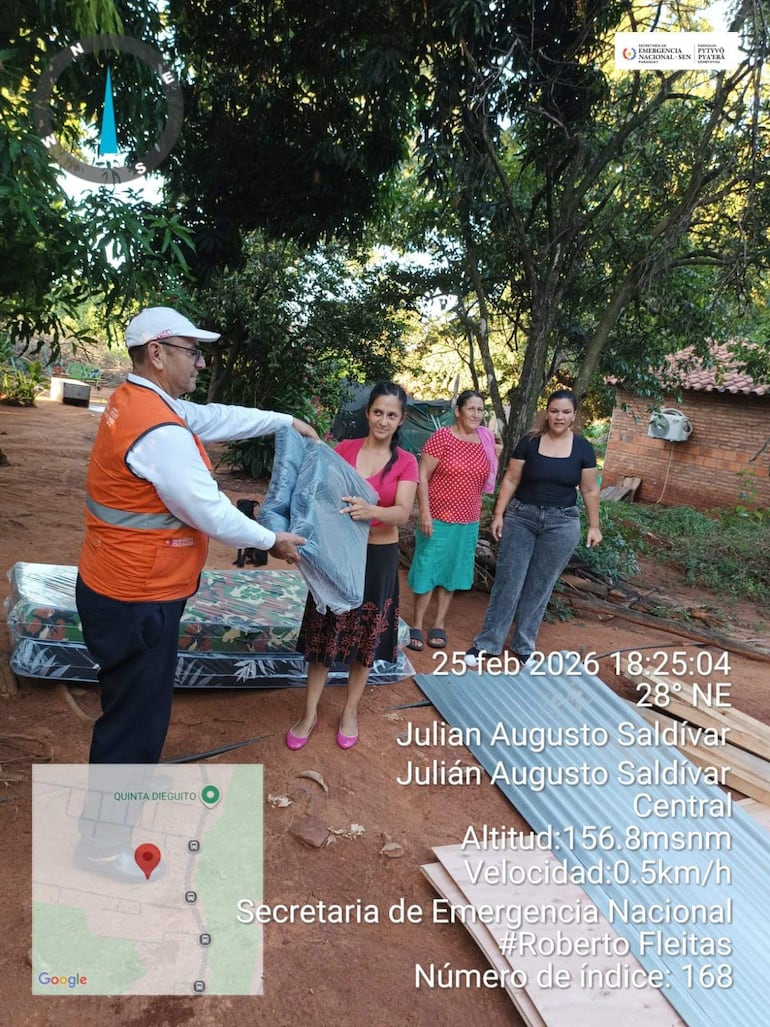 Hombre con chaleco naranja y mujer con camiseta rosa conversan mientras sostienen mantas, en un entorno comunitario.