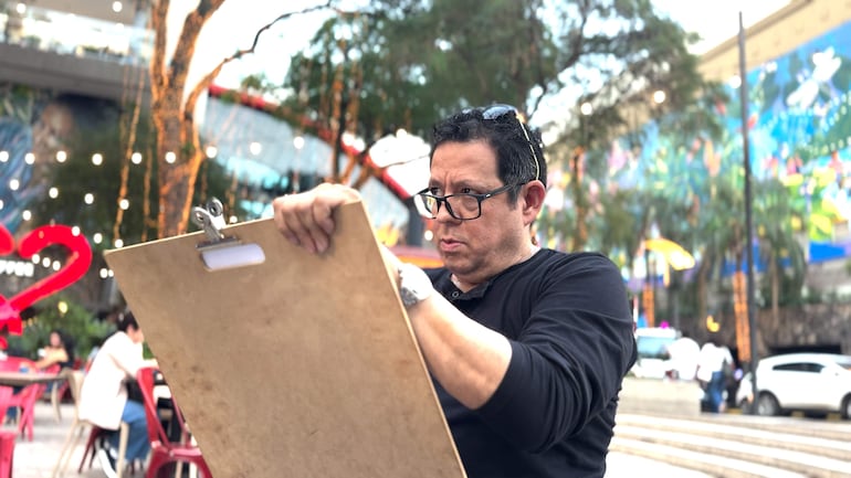 Hombre de cabello oscuro con gafas y camiseta negra sostiene un clipboard, concentrado en un entorno urbano con decoraciones luminosas.