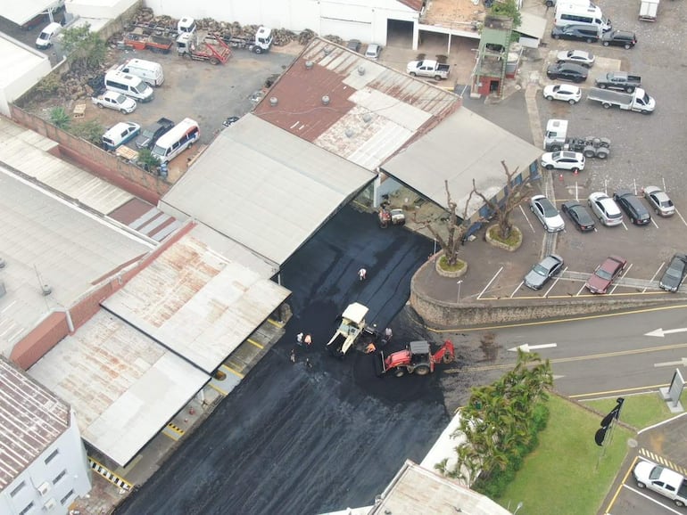 Cinco trabajadores en la calle están operando una máquina asfaltadora, concentrados en la tarea de pavimentación.