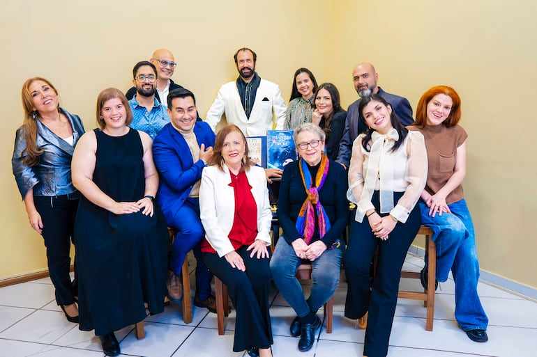 Coro de 14 personas sonriendo y posando, algunos sosteniendo libros, con fondo amarillo en evento musical.
