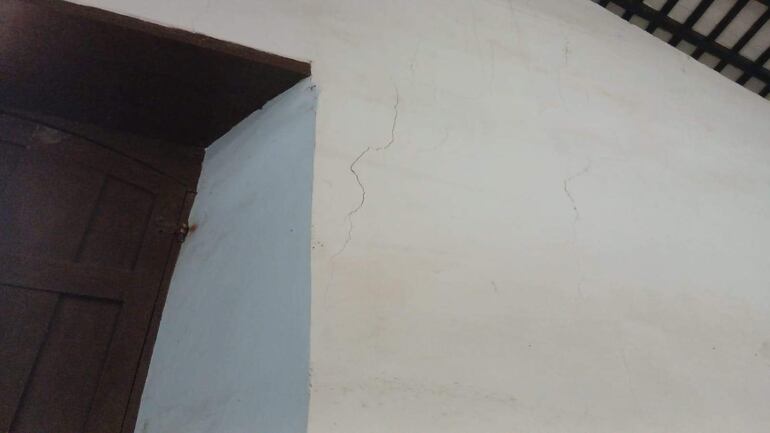 Pared interior de la Catedral con grietas visibles y marco de puerta de madera a la izquierda.