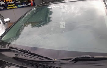 Automóvil con parabrisas dañado y grietas visibles, en un entorno urbano con otros vehículos y un negocio al fondo.