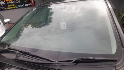 Automóvil con parabrisas dañado y grietas visibles, en un entorno urbano con otros vehículos y un negocio al fondo.