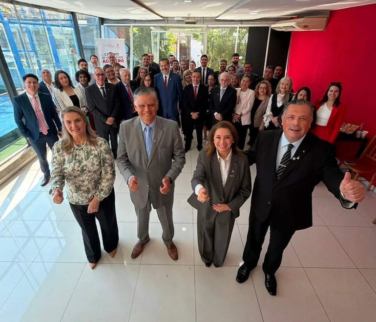 Juan Sosa Bareiro y su equipo sonríen, vistiendo trajes y blusas profesionales en un salón de eventos, mostrando pulgares hacia arriba.