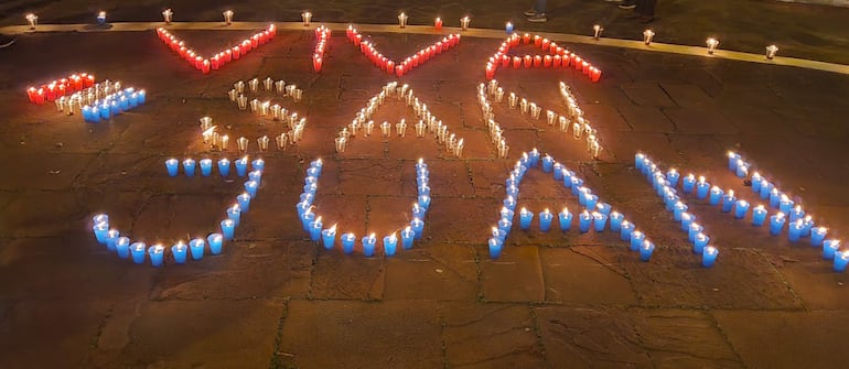 Candiles encendidos formando la frase '¡Viva San Juan!' en colores rojo y azul en la plaza bajo un cielo nocturno.