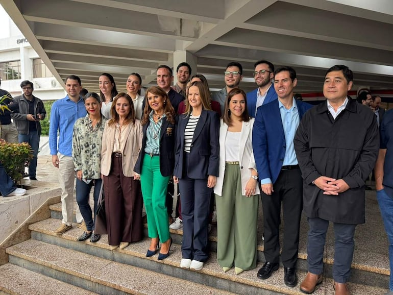 Sole Núñez en abrigo oscuro sonríe junto a su equipo en escalinata de edificio, todos con expresión alegre.