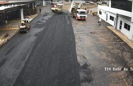 Obreros en obra vial, camiones y rodillo compactador en un ambiente nublado frente al taller T14.