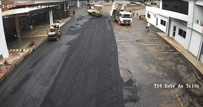 Obreros en obra vial, camiones y rodillo compactador en un ambiente nublado frente al taller T14.