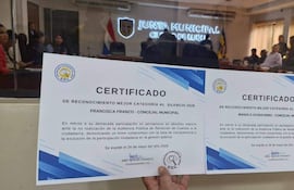 Francisca Franco y Manolo Achucarro presentan certificados de reconocimiento en un salón de actos con buena iluminación y bandera paraguaya.