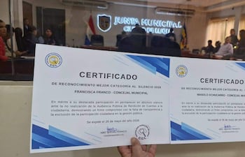 Francisca Franco y Manolo Achucarro presentan certificados de reconocimiento en un salón de actos con buena iluminación y bandera paraguaya.