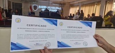 Francisca Franco y Manolo Achucarro presentan certificados de reconocimiento en un salón de actos con buena iluminación y bandera paraguaya.