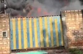 Escena de un incendio con llamas y humo saliendo de una puerta metálica azul y amarilla en un ambiente urbano.