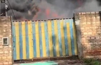 Escena de un incendio con llamas y humo saliendo de una puerta metálica azul y amarilla en un ambiente urbano.