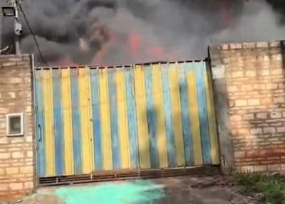 Escena de un incendio con llamas y humo saliendo de una puerta metálica azul y amarilla en un ambiente urbano.