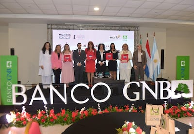 Ocho mujeres sonrientes, sosteniendo premios en un evento decorado con flores, mientras banderas de Paraguay y Argentina adornan el fondo.