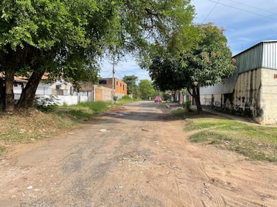 Calle de Itay con casas de ladrillo y paredes blancas, árboles a los lados y un vehículo rojo estacionado.