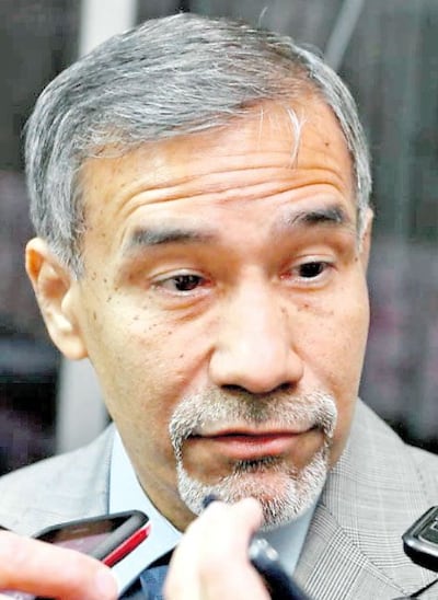 Manuel Ramírez, hombre canoso con barba, habla con micrófonos frente a él en un entorno cerrado y formal.